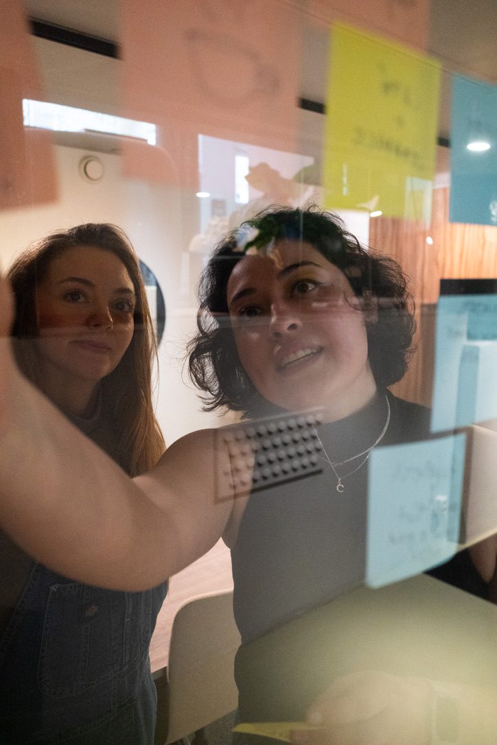 Cristina and a participant placing sticky notes on a glass wall during a Lab session